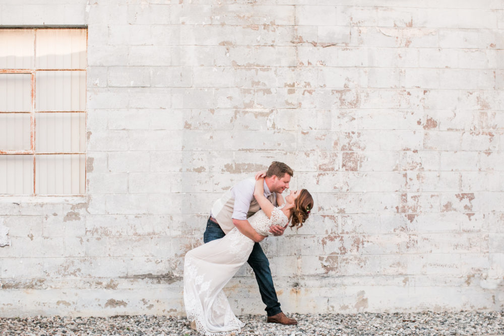 Bride and groom kiss and dip in front of white brick wall at smoky hollow studios - modern wedding venue in Los Angeles