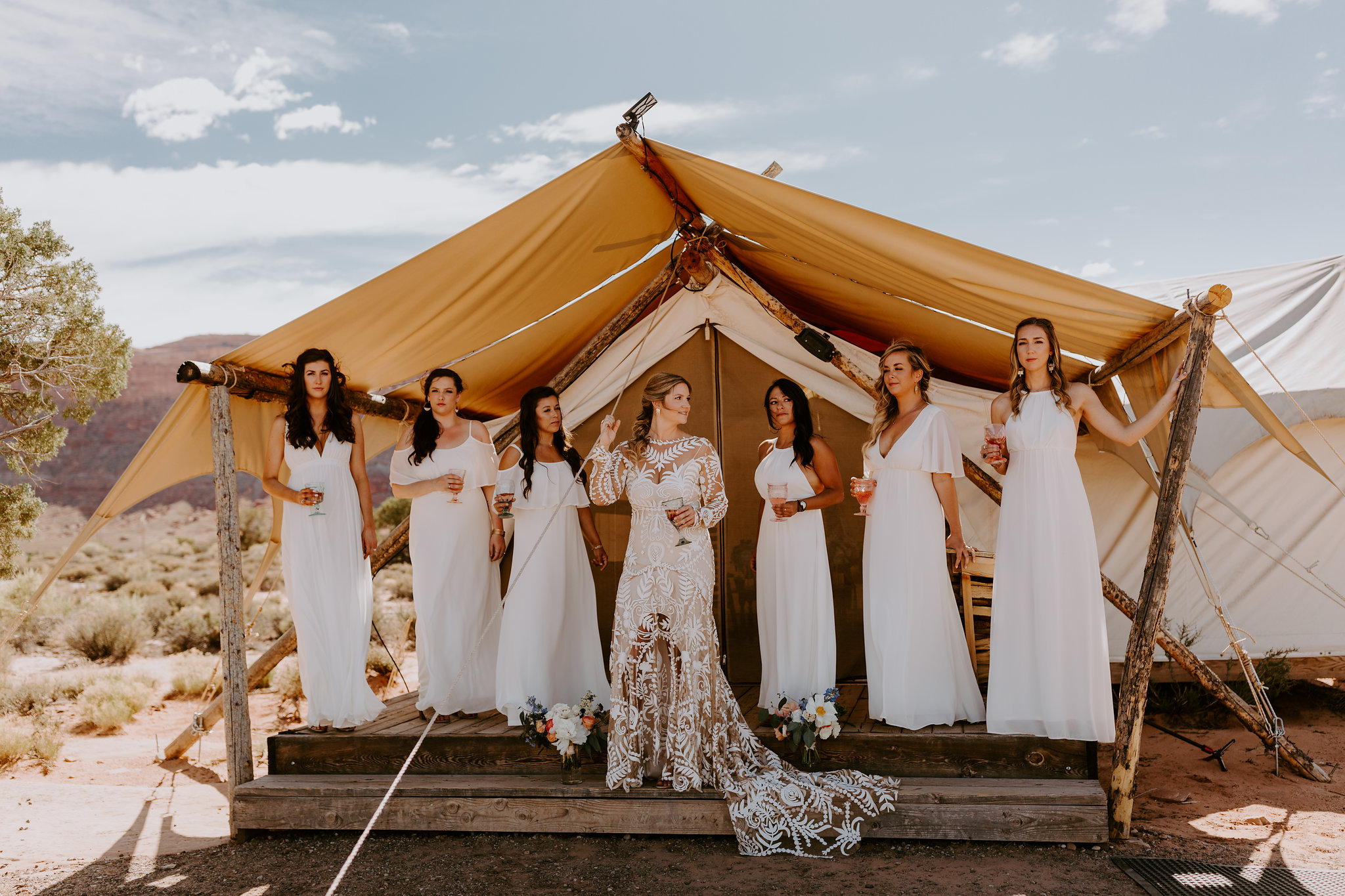 Bride and bridesmaids in all white in front of glamping tent. Desert wedding at Under Canvas Moab