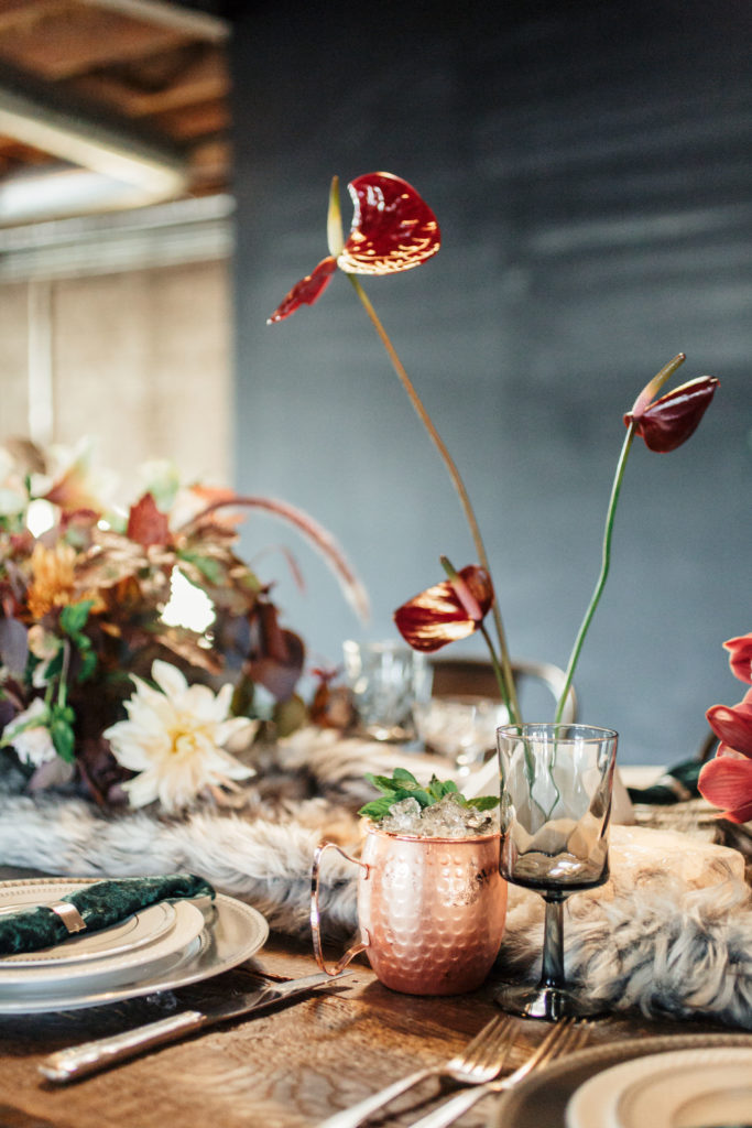 Thanksgiving table decor with faux fur table runner, geometric candle holders and velvet napkins. Copper moscow mule cup at dinner table