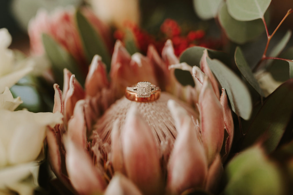 Rose gold engagement ring and band sitting on king protea flower