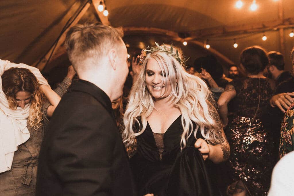 Bride and groom in all black with tattoos dance at their wedding