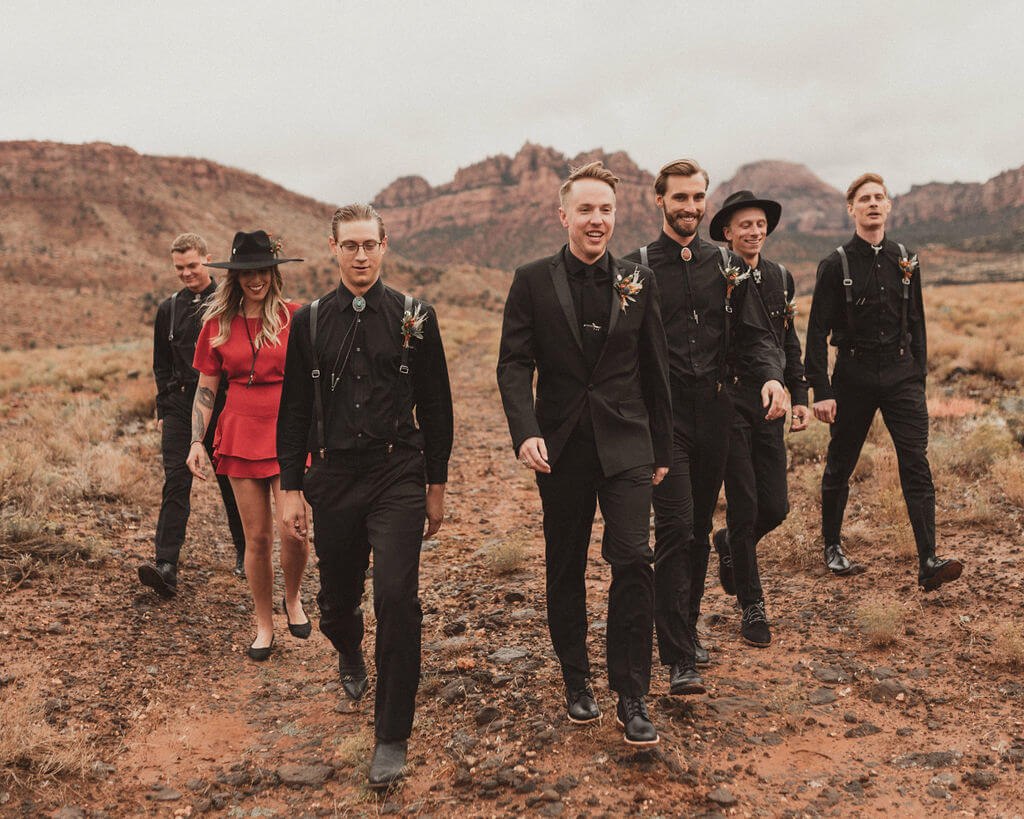 Groom in all black with groomsmen in all black and groomswoman in red. Zion Under Canvas desert wedding.