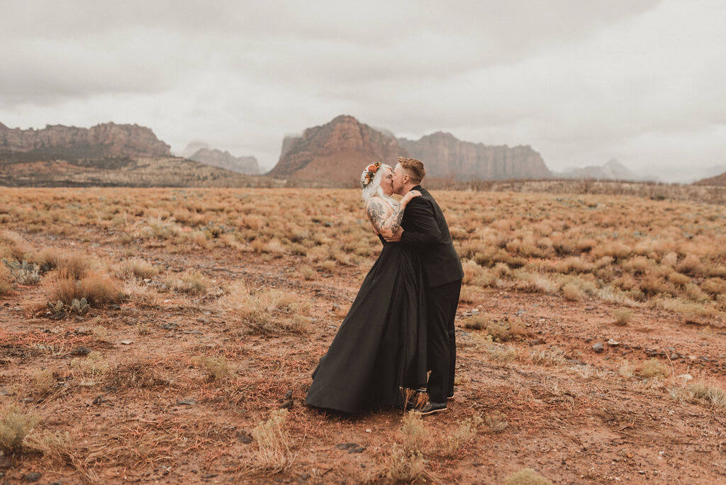 Bride and groom in all black kiss near Zion National Park before their epid 3 day glamping wedding