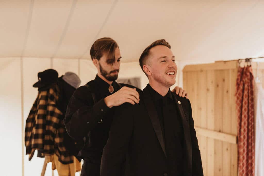 Best man helping groom put his suit on before the wedding