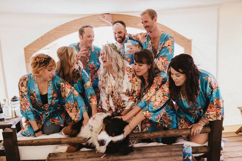 Bride and her bridesmaids and bridesman getting ready in a glamping tent with their dog Boom. Bridal party is wearing floral blue robes.