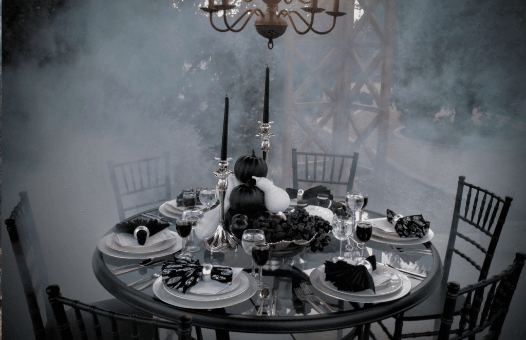 Six place settings on round table with black and white halloween table decor and pumpkins surrounded by fog.