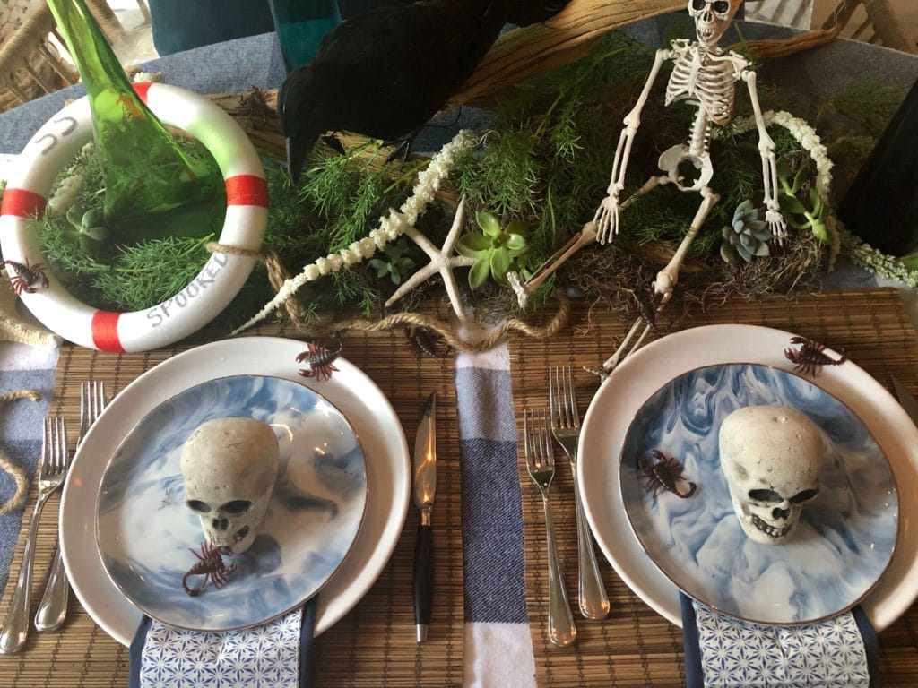 Table with two place settings of marbled navy and white plates on with scorpions and mini skulls.